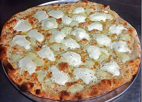 Wood-fired pizza with white cheese dollops and herbs on a crispy, golden crust