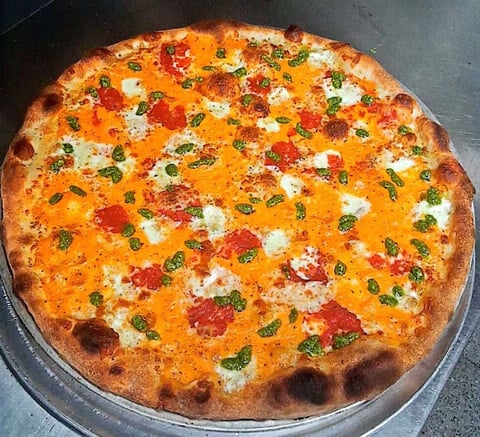Freshly baked pizza with melted cheese, pepperoni, fresh basil, and white cheese dollops on a metal pan