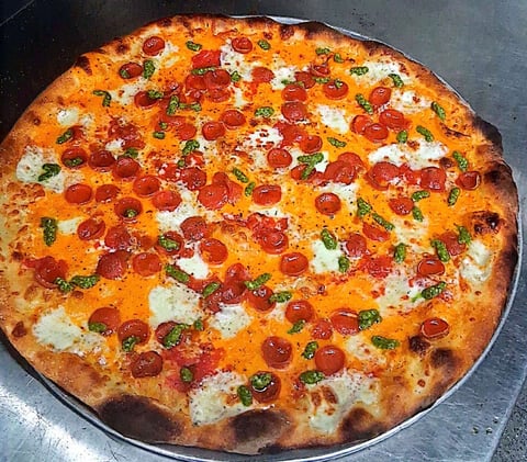 A round pizza topped with pepperoni, mozzarella cheese, and fresh basil on a dark baking surface