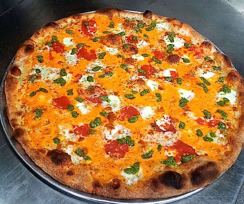 Freshly baked pizza with melted cheese, tomatoes, fresh basil, and white cheese dollops on a charred crust