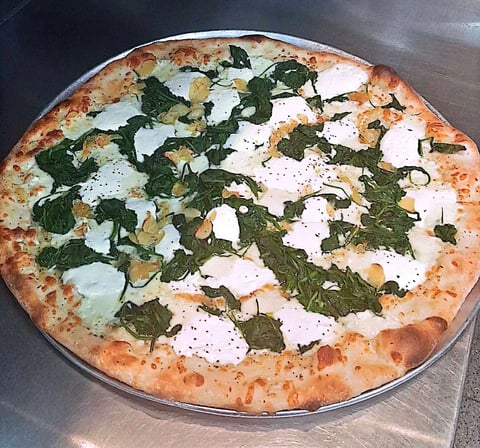 Wood-fired pizza with fresh mozzarella, arugula, and black pepper on a metal surface