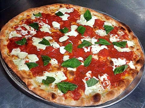 Margherita pizza with tomato sauce, fresh mozzarella, basil leaves, and a golden crust on a dark surface